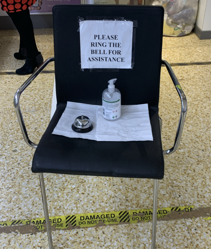 A black chair with a sign on it saying Please ring bell for assistance. A bell is on the chair