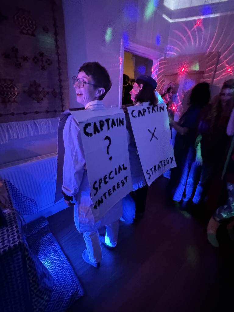 Two people dressed in cardboard outfits that say 'Captain Special Interest' and 'Captain strategy'